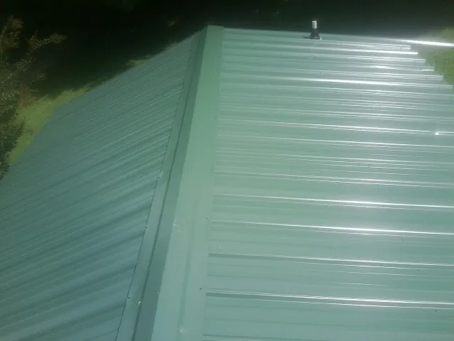 New green metal panels meeting at the ridge of a roof — Flat Roof Repair work by our crew in Louisburg
