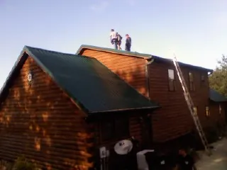 Crew on the ridge of a green metal roof on a two story log home in Louisburg