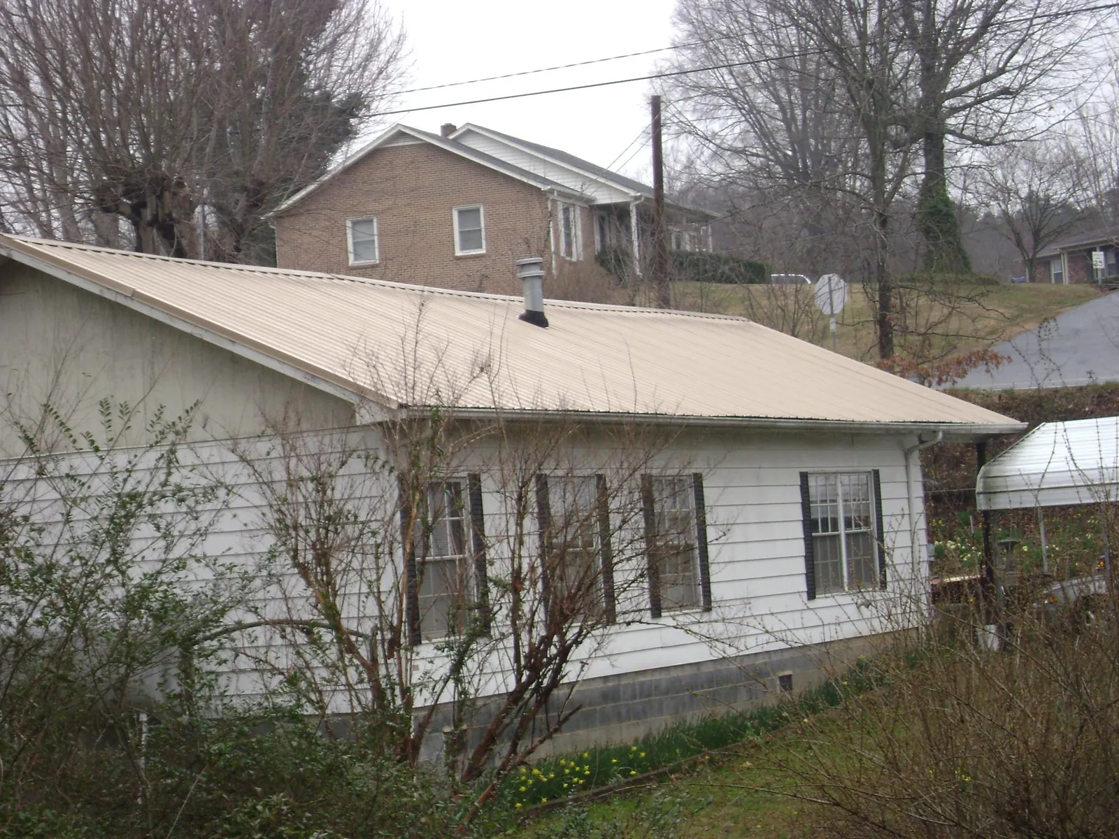 Tan metal roof on a white sided house set into a hillside — Commercial Roofing by Roofing Brothers in Louisburg
